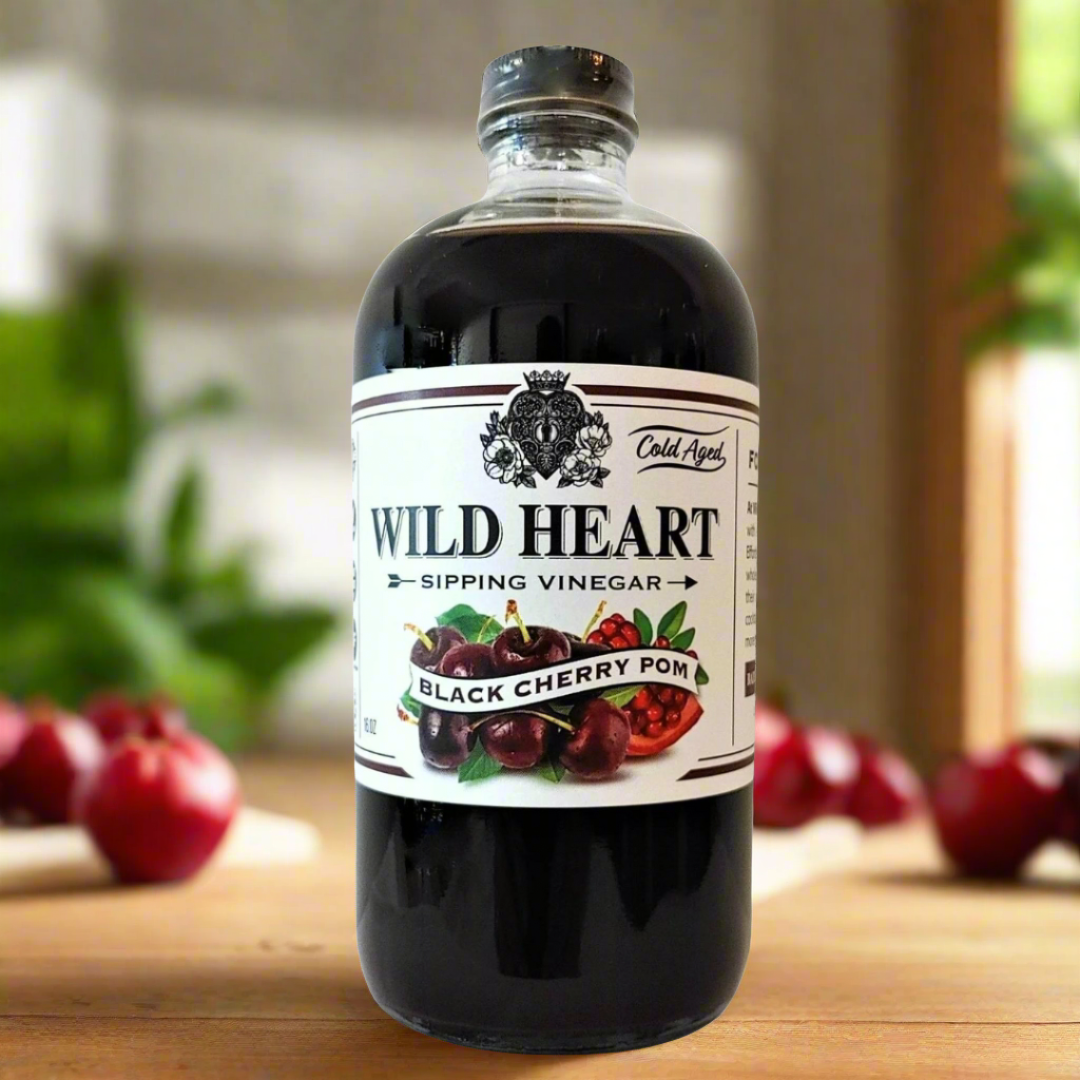 Wild Heart Black Cherry Pom sipping vinegar bottle on a kitchen counter with cherries