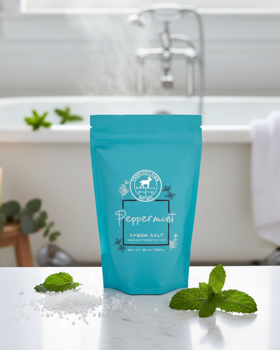 Peppermint Epsom bath salts in a 2 lb turquoise pouch beside a bathtub with fresh mint and salt crystals